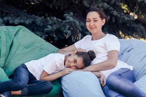 Smiling Mother And Daughter Relax On Cushions In The Park On A S Stock