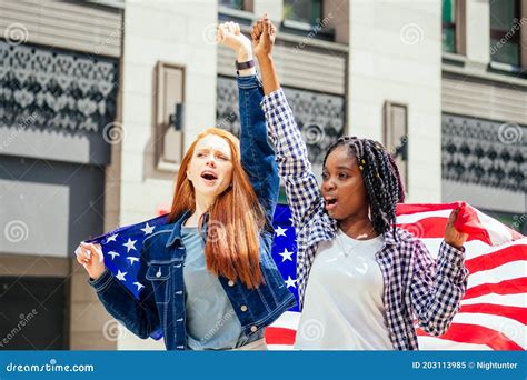 lesbian redhaired ginger woman and her african american wife holding usa flag in downtown street