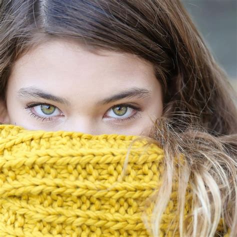 A Close Up Of A Person Wearing A Knitted Scarf Over Their Face With Her