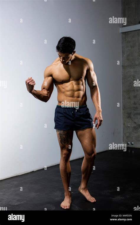 An Asian Fitness Model Flexing His Bicep Muscle And Looking At It Long