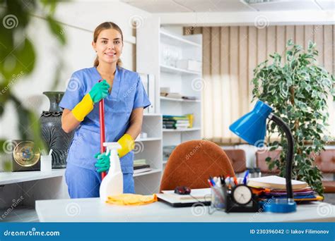 Smiling Young Female Cleaner In Uniform Ready For Cleaning In Office