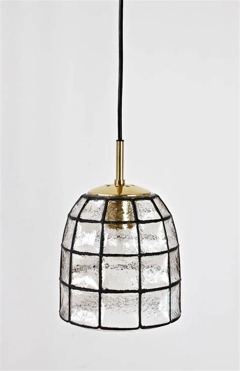 A Glass And Brass Pendant Light Hanging From A Black Cord With White Squares On It