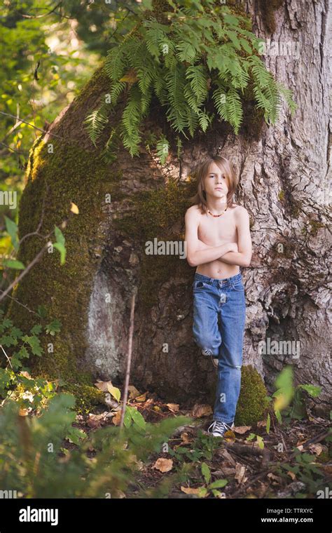 Portrait Of Shirtless Boy With Arms Crossed Standing By Tree In Forest