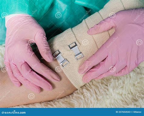 A Doctor Wearing Medical Gloves Wraps An Elastic Bandage Around The