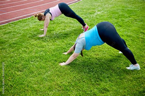 Two Young Active Fat Women Bending Over Lawn With Stretched Arms And