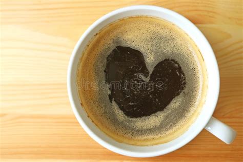 A Cup Of Hot Coffee With Heart Shaped Coffee Foam On Light Brown Wooden