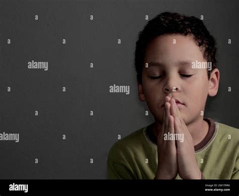 Little Boy Praying To God With Hands Together With Black Background