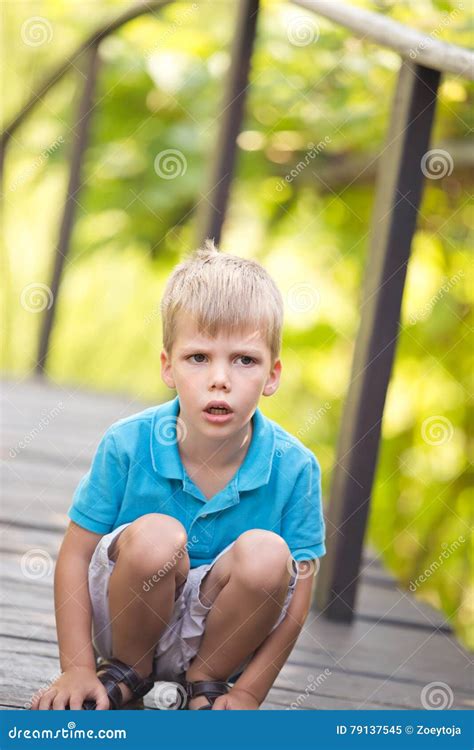 A Little Boy Kneeling Outdoor With A Serious Facial Expression Stock