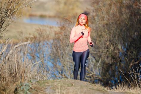 Young Woman Jogging In The Park Near The Pond In The Cold Sunny Morning