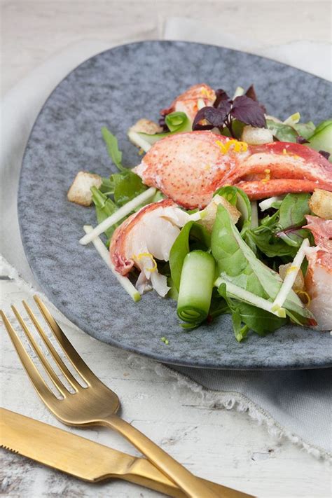 A Blue Plate Topped With Lobster Salad Next To A Fork And Knife On Top
