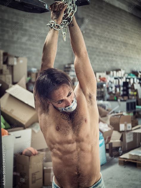Shirtless Adult Male With Tied Hands And Duct Tape On Mouth Hanging On Chains From Ceiling In