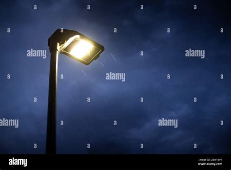 Lit Street Lamp At Twilight With Moody Blue Sky And Rain Falling