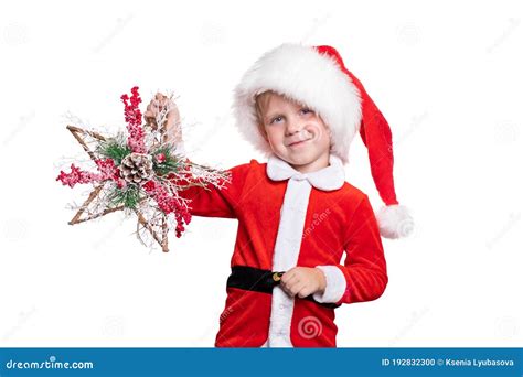 A Child Boy In A Suit And A Santa Claus Hat Holds A Wooden Star