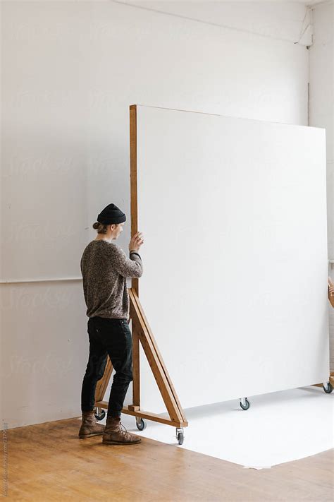 Young Man Moving A Rolling Backdrop Wall In Photo Studio By Stocksy