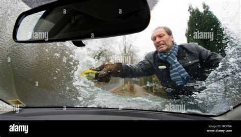 A Man Is Scraping The Ice From The Windscreen Of His Car Stock Photo