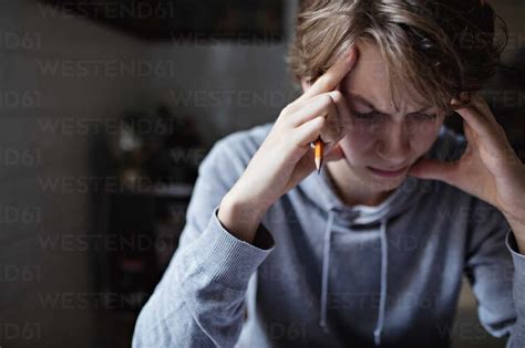 Stressed Teenage Boy With Head In Hands Studying At Home Stock Photo