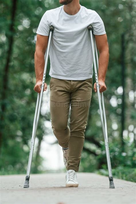 Walking In The Beautiful Park Man With Crutches Is Outdoors Stock