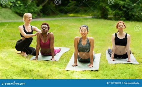 yoga teacher helping millennial girls to do pose correctly during outdoor class at park stock