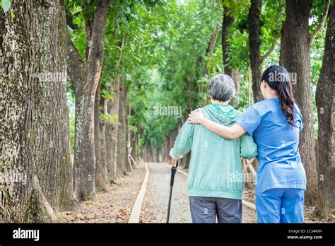 Smiling Nurse Helping Senior Woman To Walk Around The Park Stock Photo