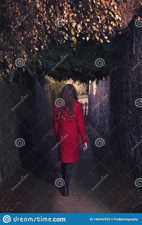 Woman In Red Coat Walking Through Dark Alley Alone Stock