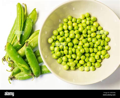 A Bowl Of Freshly Shelled Peas And Empty Pea Pods From Above On A White