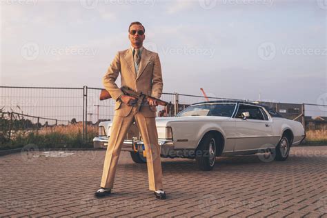Retro 1970s Gangster Holding Gun Standing In Front Of Car 1216387