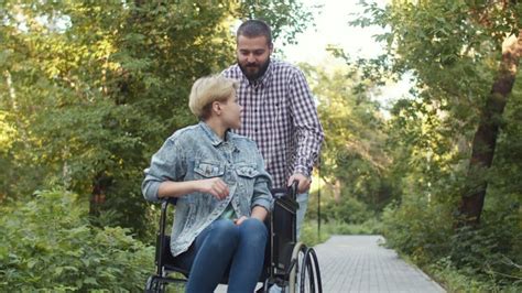Hipster Man Rolls Caucasian Disabled Woman In Wheelchair And Talks To Her Concept Of Supporting