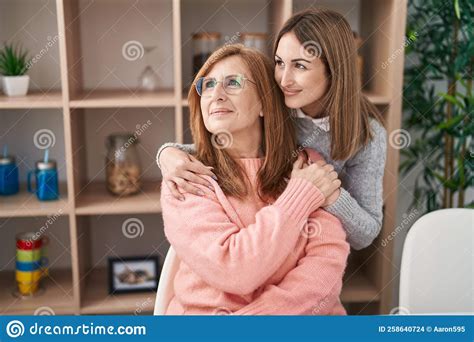 Mother And Daughter Hugging Each Other Sitting On Desk At Home Stock