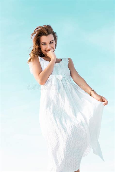 Angle View Of Smiling Beautiful Girl In White Dress Against Blue Sky