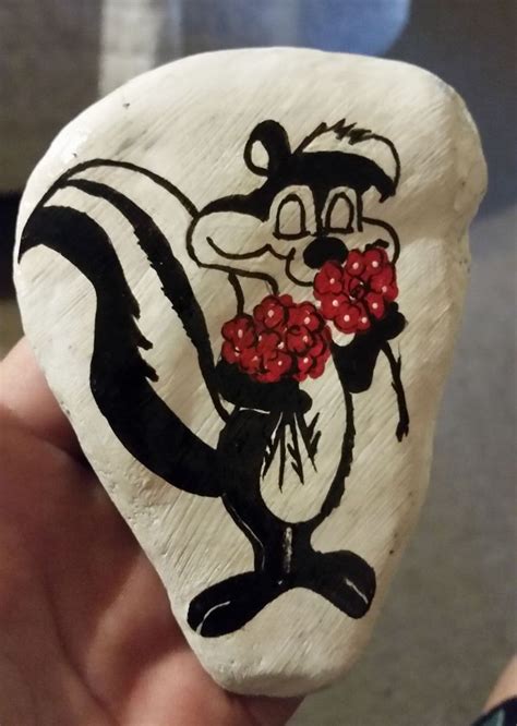 A Hand Holding A Painted Rock With An Image Of A Skunka On It