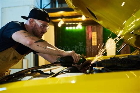 Young Repairman Bending Over Engine Of Car While Using Electric Grinder