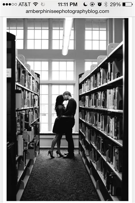 A Man And Woman Kissing In Front Of A Library Full Of Book Shelves