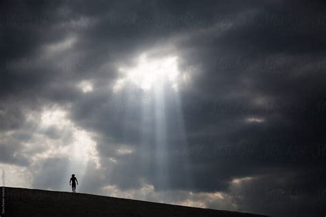 A Man Walking Across Sand Dunes As A Ray Of Light Shines Through The