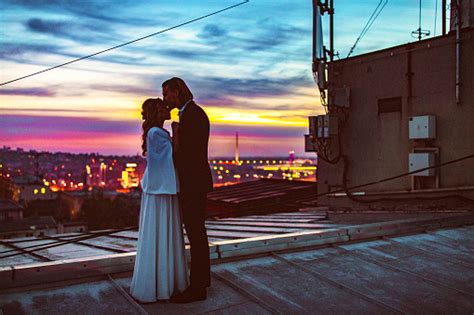 Affectionate Bride And Groom Embraces And Kisses On The Rooftop At
