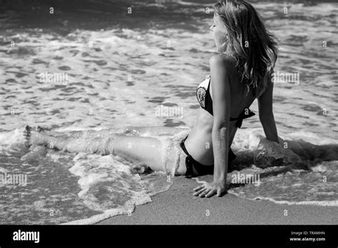 Young Blond Woman In Swimsuit At Sea Surf With Foam Sitting Under Sun Rays Monochrome Stock