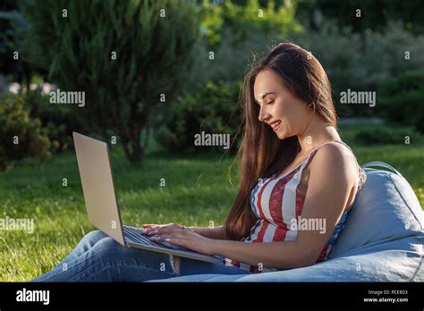Young Cute Girl With Laptop Sit On Bean Bag In Garden Or Park On