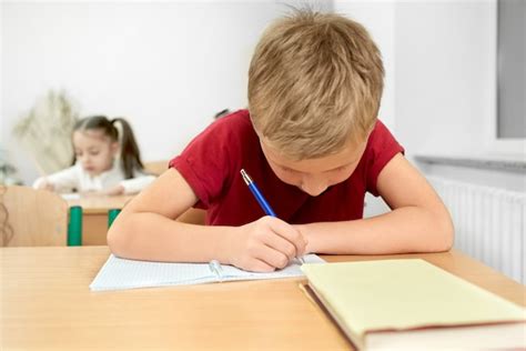 Premium Photo Schoolboy Sitting At Desk Writing With Pen In Copybook