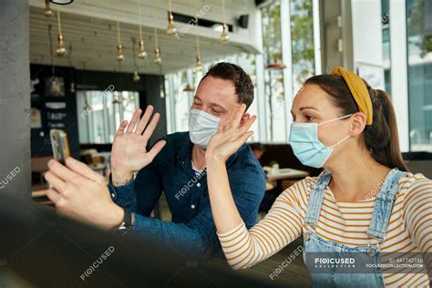 Two People Wearing Face Masks Using A Smart Phone Waving During A Face Time Call — Global