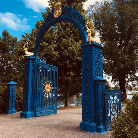 An Ornate Blue Gate With Statues On Top And Trees In The Backgroung