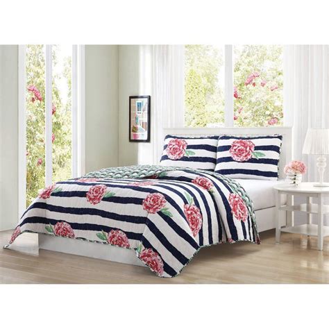 A White Bed With Pink Flowers On It And Blue Striped Comforter Set In