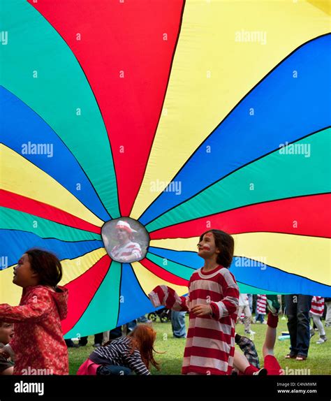 Children Play Beneath A Colourful Parachute Held Aloft By Adults On The