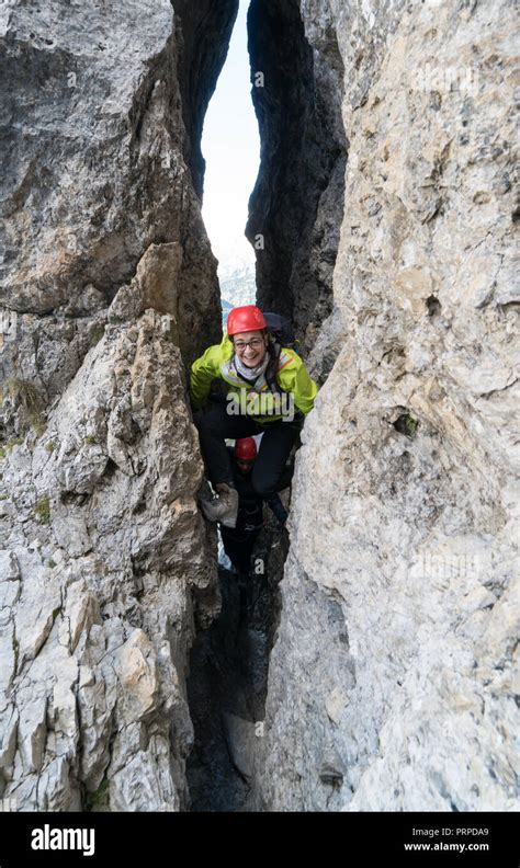 Two Young Female Mountain Climbers Climb Through A Narrow Crack On A