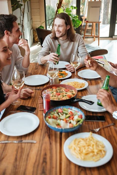 Group Of Cheerful Friends Eating And Talking At The Table Stock Photo