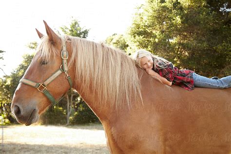 Portrait Of Little Girl Lying On Horse In Nature Smiling By Stocksy