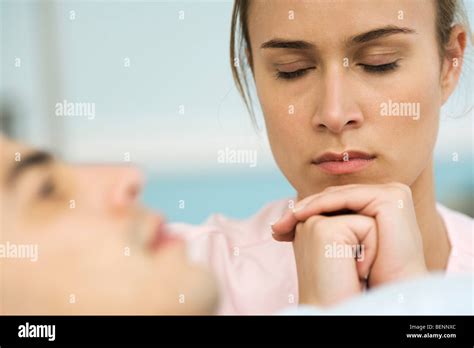 Woman Sitting Beside Sleeping Man Hands Clasped In Front Of Face Eyes