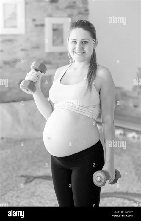 Retrato En Blanco Y Negro De Mujer Embarazada Sonriente Posando Con Pesas En El Gimnasio