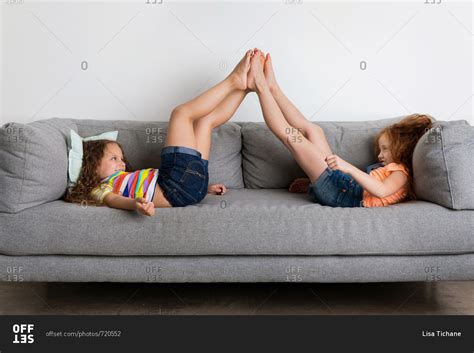 Two Girls Lying On Gray Sofa Touching Feet Stock Photo Offset