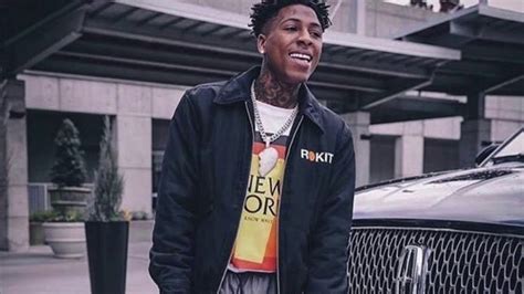 Smiley Nba Youngboy Is Wearing White Yellow T Shirt And Black Overcoat