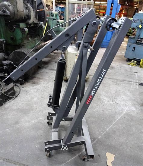 The secondary workshop with numerous worktables, an engine hoist, a hydraulic car lift tyre rack found on the secondary workshop, as well as an engine hoist and several bumpers, hoods, catalysts. PITTSBURGH 2-TON CAPACITY FOLDING ENGINE HOIST
