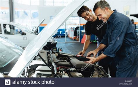 Two Happy Automobile Mechanics Doing Car Engine Checkup With A Device